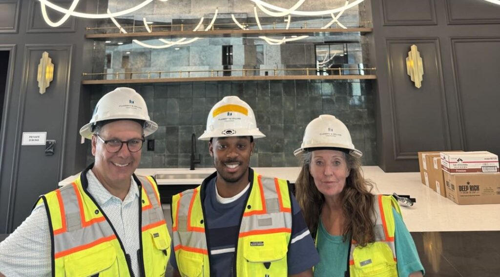 Cross Builds team member with two colleagues in hard hats and safety vests, smiling inside a finished commercial lounge at a Flaherty & Collins Properties development.