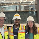 Cross Builds team member with two colleagues in hard hats and safety vests, smiling inside a finished commercial lounge at a Flaherty & Collins Properties development.
