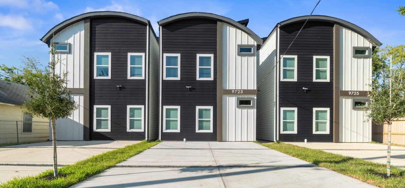 Front exterior of a modern multi-unit residential property featuring black and gray siding, curved rooflines, and concrete driveways.