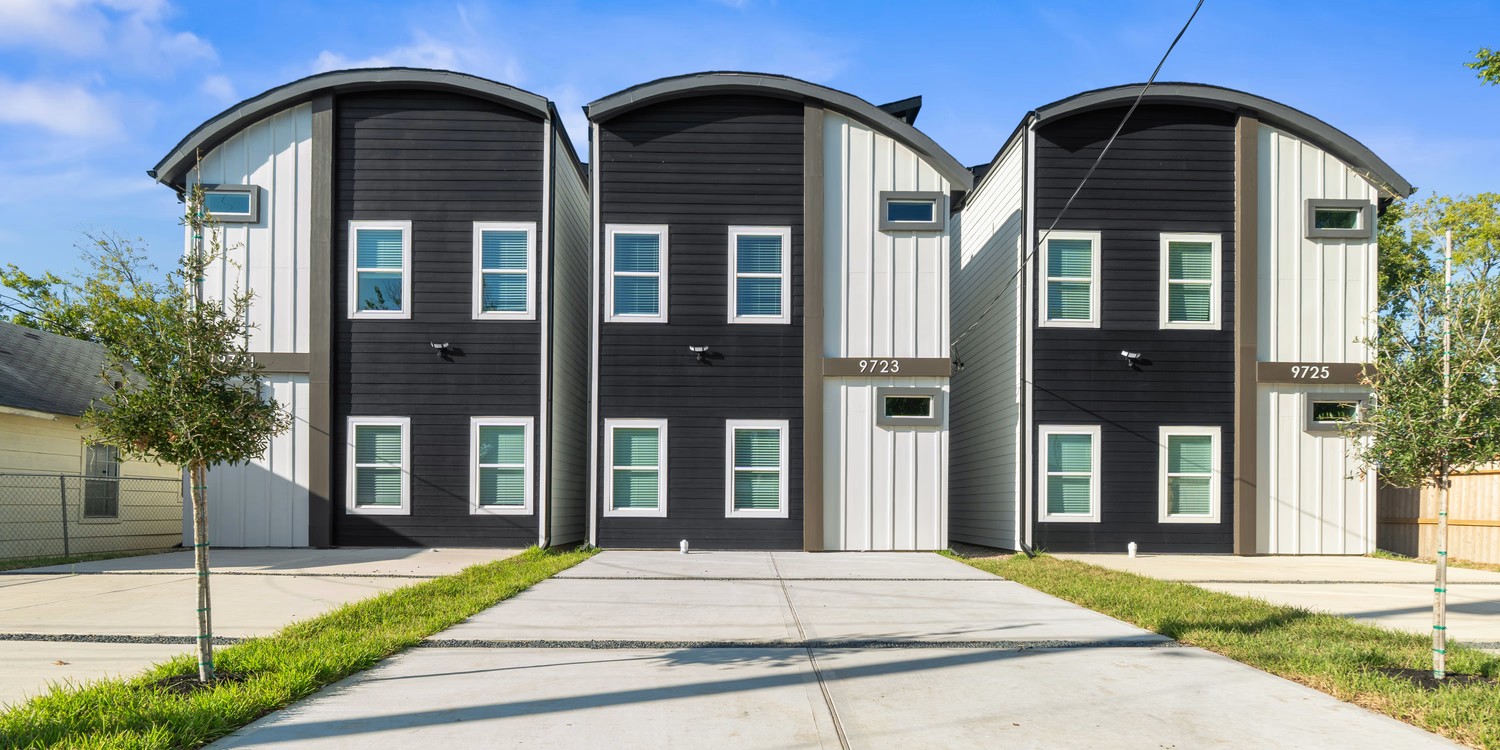 Front exterior of a modern multi-unit residential property featuring black and gray siding, curved rooflines, and concrete driveways.